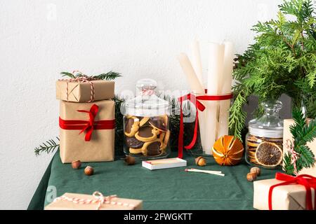 Tavolo festoso decorato Natale o Capodanno, rami thuja e abete rosso, candele e fette di agrumi secchi, biscotti al cioccolato in un vaso Foto Stock