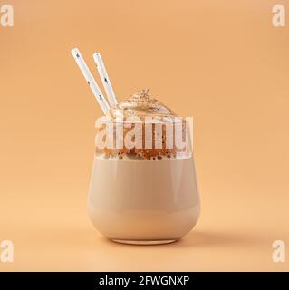 Caffè Dalgona in un bicchiere trasparente con paillette su sfondo arancione. Vista laterale, primo piano. Foto Stock