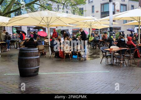 Münster, NRW, Germania, 22 maggio 2021. La gente sembra felice di avere il loro cibo e bere fuori, nonostante la pioggia. Le folle si riuniscono nel centro storico di Münster, nonostante la pioggia battente, poiché diventa la prima città del Nord Reno-Westfalia ad essere autorizzata ad aprire bevande e ristoranti al coperto (con test o vaccinazione negativi), e lo shopping senza un test o appuntamento (ma i numeri sono limitati). Münster attualmente ha uno dei più bassi tassi di incidenza di covid in NRW a 17/100k ed è diventato una 'regione del model' per provare la lenta riapertura dei luoghi di ospitalità. Foto Stock