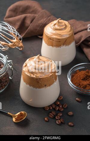 Caffè dalgona coreano in due bicchieri trasparenti su sfondo marrone. Vista verticale. Foto Stock