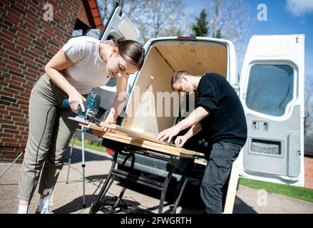 03 aprile 2021, bassa Sassonia, Großenmeer: Greta Thomas e Hannes Wehrmann stanno segando legno di fronte alla loro Mercedes-Benz Sprinter, che la coppia sta convertendo in un campervan con il proprio lavoro. Foto: Hauke-Christian Dittrich/dpa Foto Stock