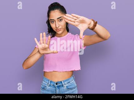 Ragazza ispanica adolescente con dentisti che indossano abiti casual facendo cornice utilizzando mani palmi e dita, fotocamera prospettiva Foto Stock