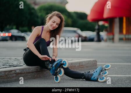 Felice giovane donna mette sui pattini di rolerskates che vanno a cavalcare i rolles in luogo urbano ha l'esercizio regolare va dentro per pericoloso lo sport regola i lacci Foto Stock