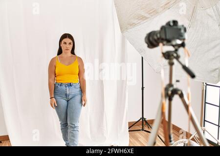 Giovane bella donna ispanica che si pone come modello in studio di fotografia scettica e nervosa, accigliata sconvolto a causa del problema. Persona negativa. Foto Stock