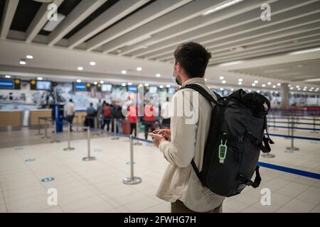 Regole di volo durante la pandemia di Covid-19 solo in maschera protettiva. Nuovo concetto normale. Uomo mascherato con telefono in mano e zaino in linea con Foto Stock