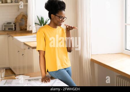 Donna casual africana parla al telefono su un altoparlante a casa. Giovane ragazza nera registra il messaggio vocale Foto Stock