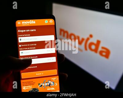 Persona titolare cellulare con pagina web della società di noleggio auto brasiliana Movida Participacoes SA su schermo con logo. Mettere a fuoco il centro del display del telefono. Foto Stock