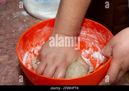 Un uomo produce pasta di pane fatta in casa in una grande ciotola. Pasta per dolci deliziosi fatti in casa da vicino. Foto Stock