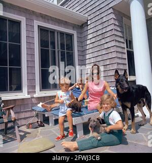 14 agosto 1963 Hyannis Port – Squaw Island - il presidente John F. Kennedy (parlando al telefono, indossando occhiali da sole), First Lady Jacqueline Kennedy, e i loro figli, Caroline Kennedy e John F. Kennedy, Jr., siedono con i loro cani, Wolf, White Tips, Blackie, e Clipper, A casa Brambletyde su Squaw Island, Hyannis Port, Massachusetts. Foto Stock