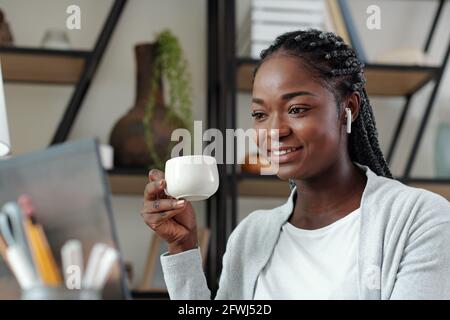 Ritratto di gioiosa giovane donna d'affari che beve caffè e videochiamata colleghi a discutere lo sviluppo dell'azienda Foto Stock