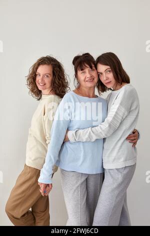 Allegra madre adulta abbracciando affascinanti giovani figlie mentre si sta in piedi sfondo bianco in studio e guardando la fotocamera Foto Stock