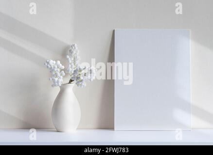 Luce del sole con ombre e linee su tela vuota o foglio, vaso, piante decorative della casa su una scrivania. Interni bianchi, minimal mockup con spazio per Foto Stock