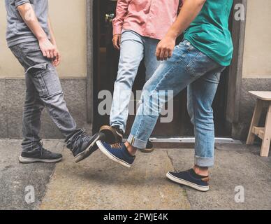 Tre amici si incontrano di fronte a una cantina. Un nuovo saluto per evitare la diffusione del coronavirus. Invece di scuotere le mani, loro bump i piedi insieme Foto Stock