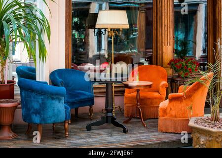 la terrazza street cafe' con poltrone dai colori tenui e tavoli rotondi su pavimento in legno vicino alla finestra con una porta d'ingresso e fiori con un decorativo Foto Stock