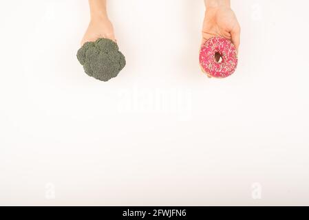 Confronto delle abitudini alimentari. Donna che tiene broccoli e ciambella su sfondo bianco Foto Stock