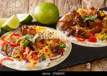 Tacos piccanti con pancia di maiale alla griglia, salsa vegetale, primo piano di formaggio su una tavola di ardesia sul tavolo. Orizzontale Foto Stock