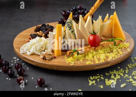 Piatto di formaggi servito con uva, marmellata, fichi, cracker e noci su fondo di pietra scuro Foto Stock