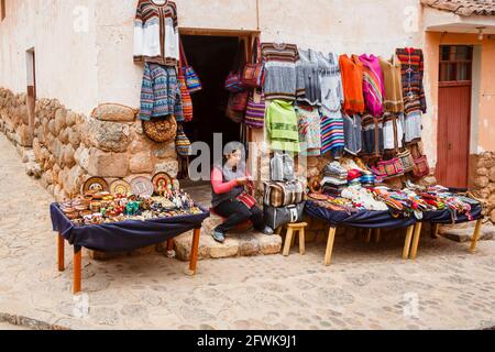 Donna locale Quechua seduta all'ingresso di un negozio di souvenir turistico, Chinchero, un villaggio andino rustico, Valle Sacra, Urubamba, Cusco Regione Perù Foto Stock