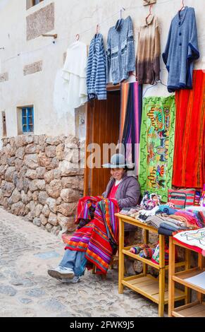 Donna locale Quechua seduta all'ingresso di un negozio di souvenir turistico a Chinchero, un villaggio andino rustico, Valle Sacra, Urubamba, Cusco, Perù Foto Stock