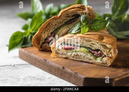 Panino croissant con cetriolo, avocado, pomodoro, spinaci, pastrami di manzo, salsa su tavola di legno. Messa a fuoco selettiva Foto Stock