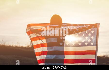Una giovane donna detiene la bandiera nazionale americana in un campo al tramonto. 4 luglio, giorno dell'Indipendenza. Concetto di libertà americana. Messa a fuoco selettiva Foto Stock