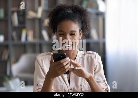 Gioiosa giovane africana mista razza donna guardando lo schermo del telefono. Foto Stock