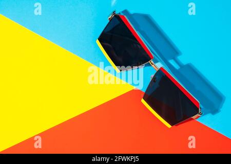 Occhiali da sole funky su sfondo giallo brillante, blu e rosso con ombra, vista dall'alto Foto Stock