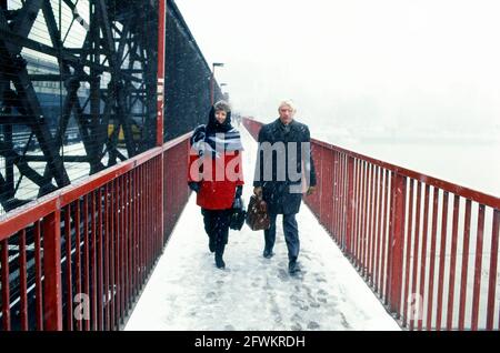 Due persone che attraversano il Tamigi, Londra, sul ponte pedonale lungo il ponte ferroviario Hungerford (da quando sostituito), in caduta di neve Foto Stock