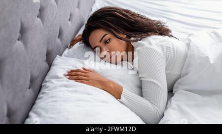 Donna nera depressa giacente a letto da sola e sconvolto Foto Stock