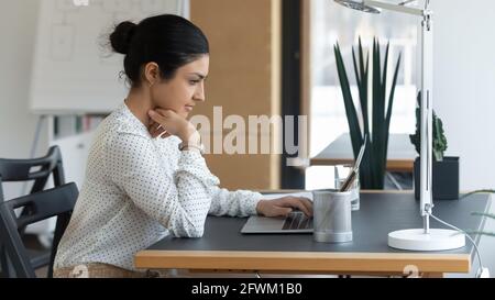 Vista laterale, uomo d'affari indiano sicuro che guarda lo schermo del computer portatile Foto Stock