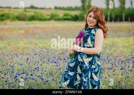 Colpo medio di donna incinta felice che tiene un bouquet di lavanda nel campo Foto Stock