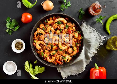 Jambalaya in stile creolo con pollo, salsicce affumicate e verdure in padella su fondo di pietra nera. Vista dall'alto, disposizione piatta, primo piano Foto Stock