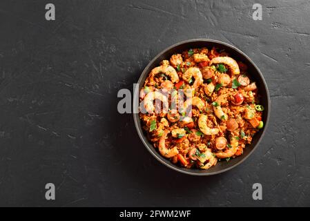 Jambalaya in stile creolo con pollo, salsicce affumicate e verdure in padella su sfondo di pietra nera con spazio libero per il testo. Vista dall'alto, disposizione piatta Foto Stock