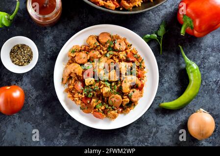 Creola jambalaya con riso, salsicce affumicate, carne di pollo e verdure su piatto su fondo di pietra blu. Vista dall'alto, disposizione piatta Foto Stock