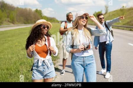 Gruppo di giovani amici positivi che camminano lungo l'autostrada, facendo foto, divertendosi insieme all'aria aperta Foto Stock