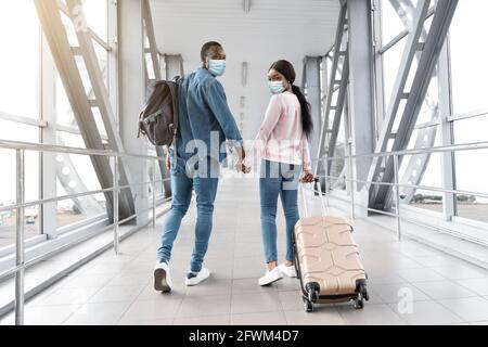 Viaggi durante Coronavirus. Coppia nera in maschere Mediche Passeggiate al Terminal dell'Aeroporto Foto Stock