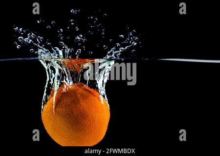 un'arancia cadde nell'acqua con spruzzi e bolle Foto Stock