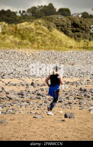 Porthcawl, Galles - 2017 agosto: Persona che fa jogging attraverso la spiaggia a Newton Bay vicino Porthcawl nel Galles del Sud. Foto Stock