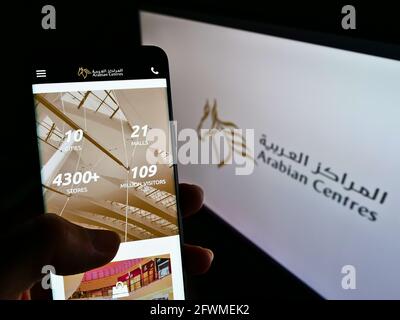 Persona che tiene il cellulare con la pagina web dell'operatore del centro commerciale Arabian Centers Company sullo schermo davanti al logo. Mettere a fuoco il centro del display del telefono. Foto Stock