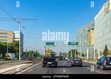 Vista della città. Auto sulla strada, tram rotaie. Scala gialla nel vano di carico del veicolo per passeggeri. Vista posteriore. Ai lati della strada vi sono edifici alti Foto Stock