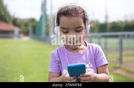 felice latina ragazza utilizzando smartphone e casco sul campo sportivo Foto Stock