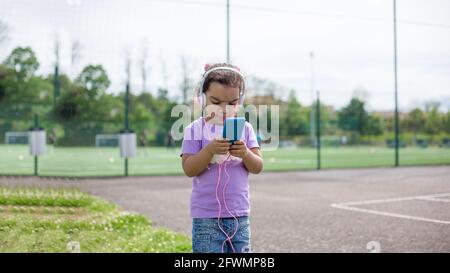 felice latina ragazza utilizzando smartphone e casco sul campo sportivo Foto Stock