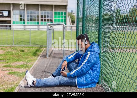 giovane latino che ascolta la musica con casco e intelligente telefono in campo sportivo Foto Stock