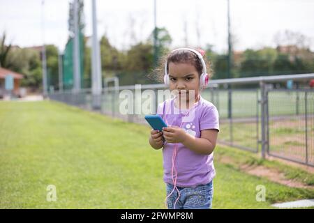 felice latina ragazza utilizzando smartphone e casco sul campo sportivo Foto Stock