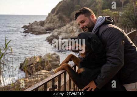 uomo che gode di vista mare con il suo cane rottweiler Foto Stock