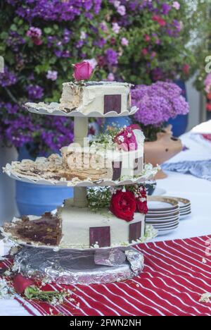 Torta a tre piani mangiata a metà su un tavolo con rose e cioccolato Foto Stock