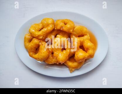 Picarones, dessert peruviano a base di Squash e patate dolci e serviti in forma di ciambella con sciroppo di Panela su un tavolo bianco Foto Stock