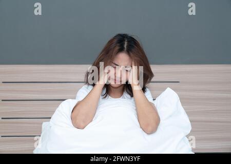 Giovani donne asiatiche che si trovano a letto tenendo la testa avendo un forte mal di testa forse emigra al mattino sul letto Foto Stock