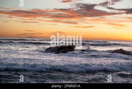 Le onde si tuffano su una roccia sotto un tramonto suggestivo e colorato su una spiaggia sulla costa pacifica della Costa Rica. Foto Stock