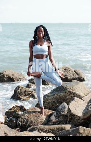 Sorridente giovane donna abbastanza in forma in piedi in albero posa su spiaggia rocciosa Foto Stock